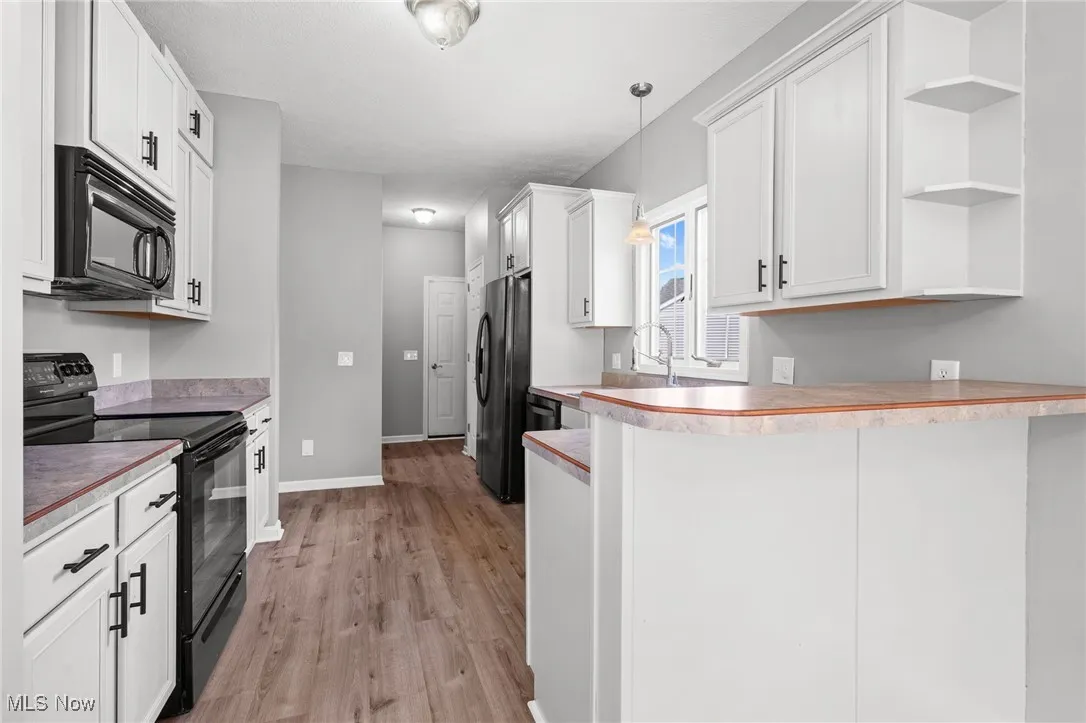 Kitchen featuring black appliances, open shelves, light wood-style flooring, a peninsula, and light countertops