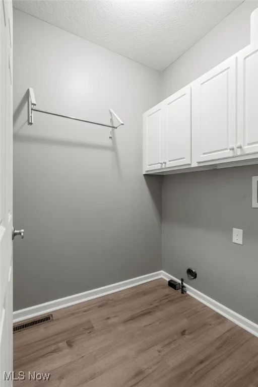 Laundry area featuring cabinet space, wood finished floors, gas dryer hookup, a textured ceiling, and washer hookup