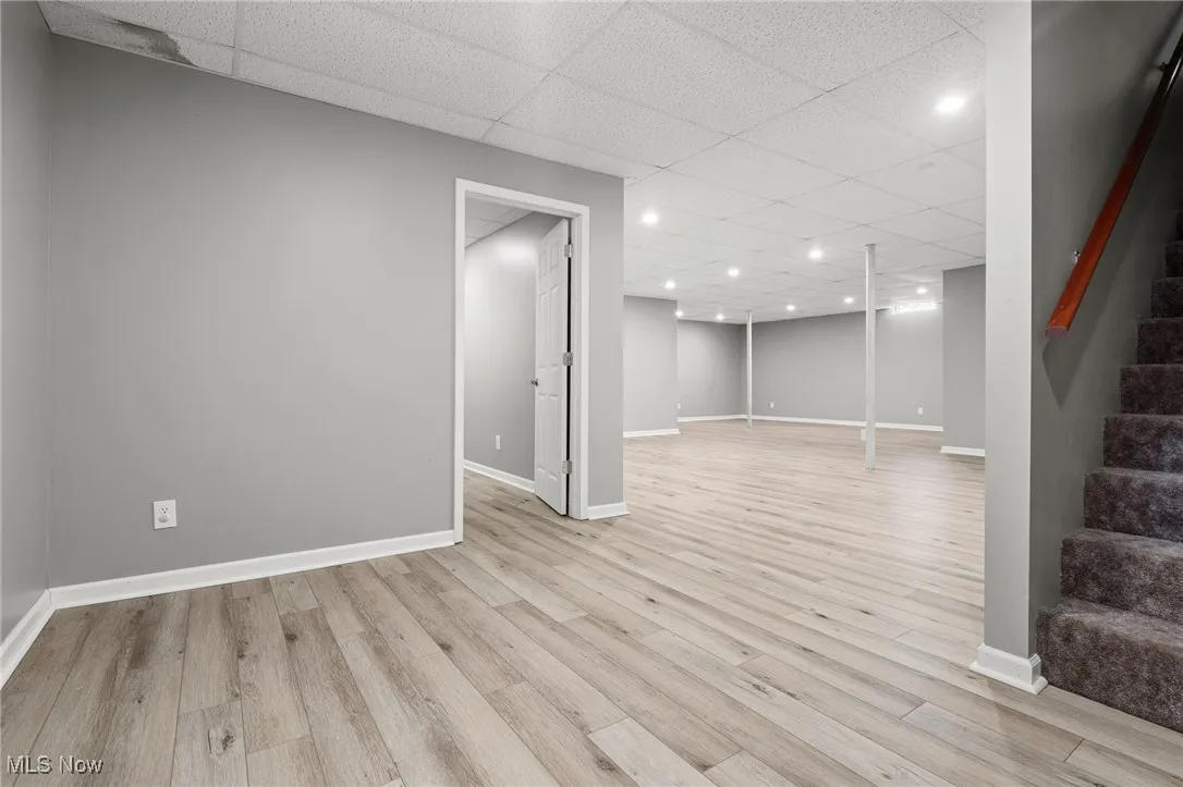 Finished basement featuring stairs, a drop ceiling, light wood-style flooring, and recessed lighting