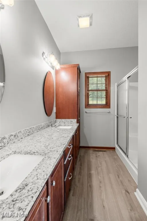 Full bathroom featuring wood finished floors, double vanity, and a shower with door