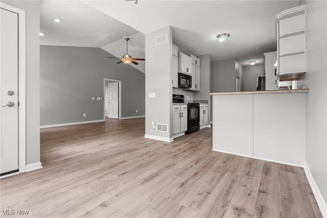 Kitchen with black appliances, open floor plan, a ceiling fan, lofted ceiling, and light wood-style flooring