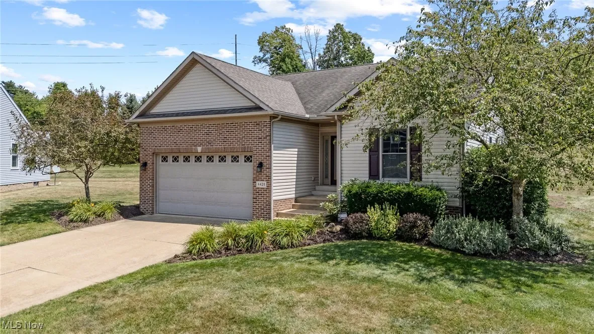 Ranch-style house featuring concrete driveway, an attached garage, brick siding, a front lawn, and roof with shingles