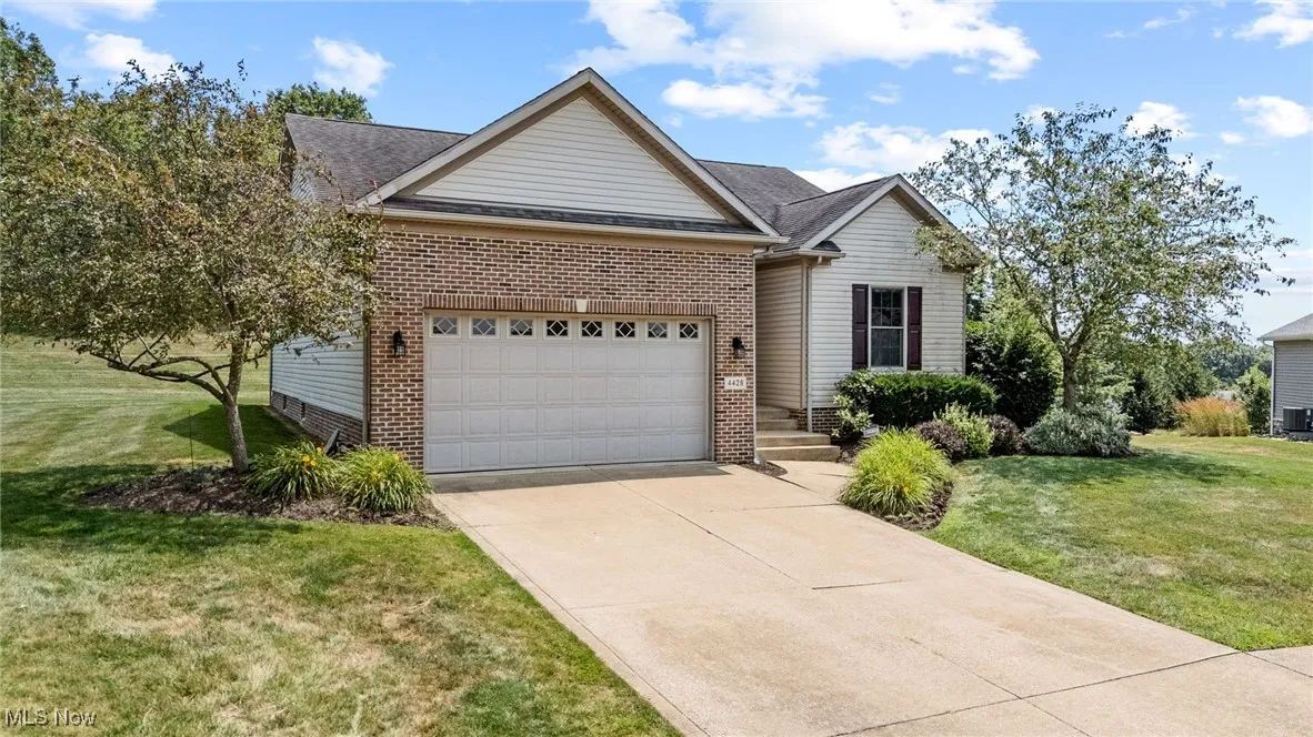 Ranch-style house featuring an attached garage, concrete driveway, brick siding, and a front lawn