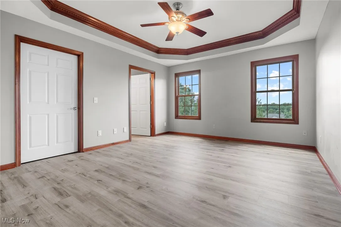 Unfurnished bedroom with a raised ceiling, crown molding, multiple windows, and light wood-style flooring