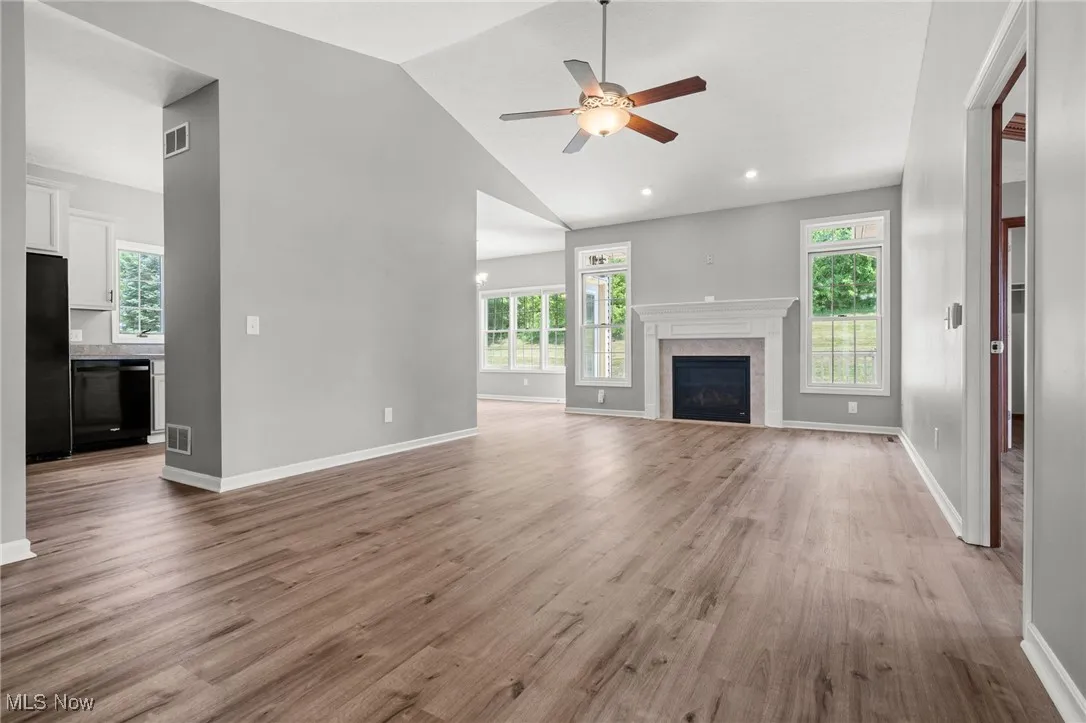 Unfurnished living room with a ceiling fan, light wood finished floors, high vaulted ceiling, and a fireplace