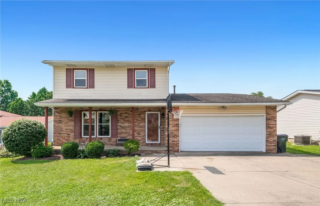 Traditional home featuring driveway, a garage, a front yard, brick siding, and a porch