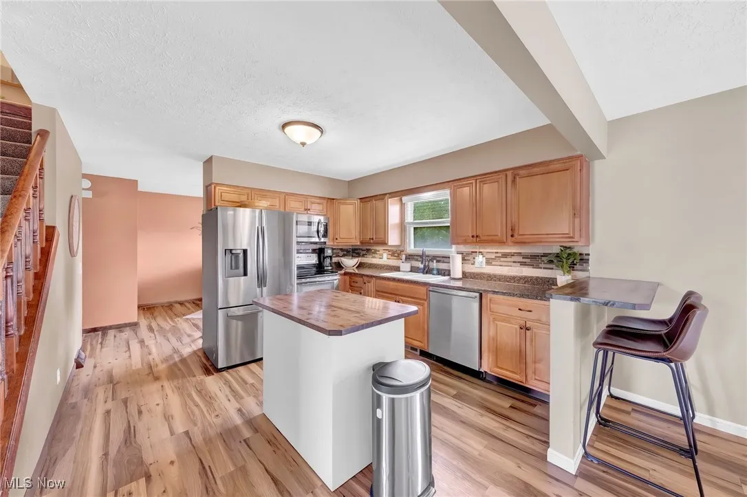 Kitchen featuring stainless steel appliances, light brown cabinets, tasteful backsplash, light wood-style flooring, and a breakfast bar area