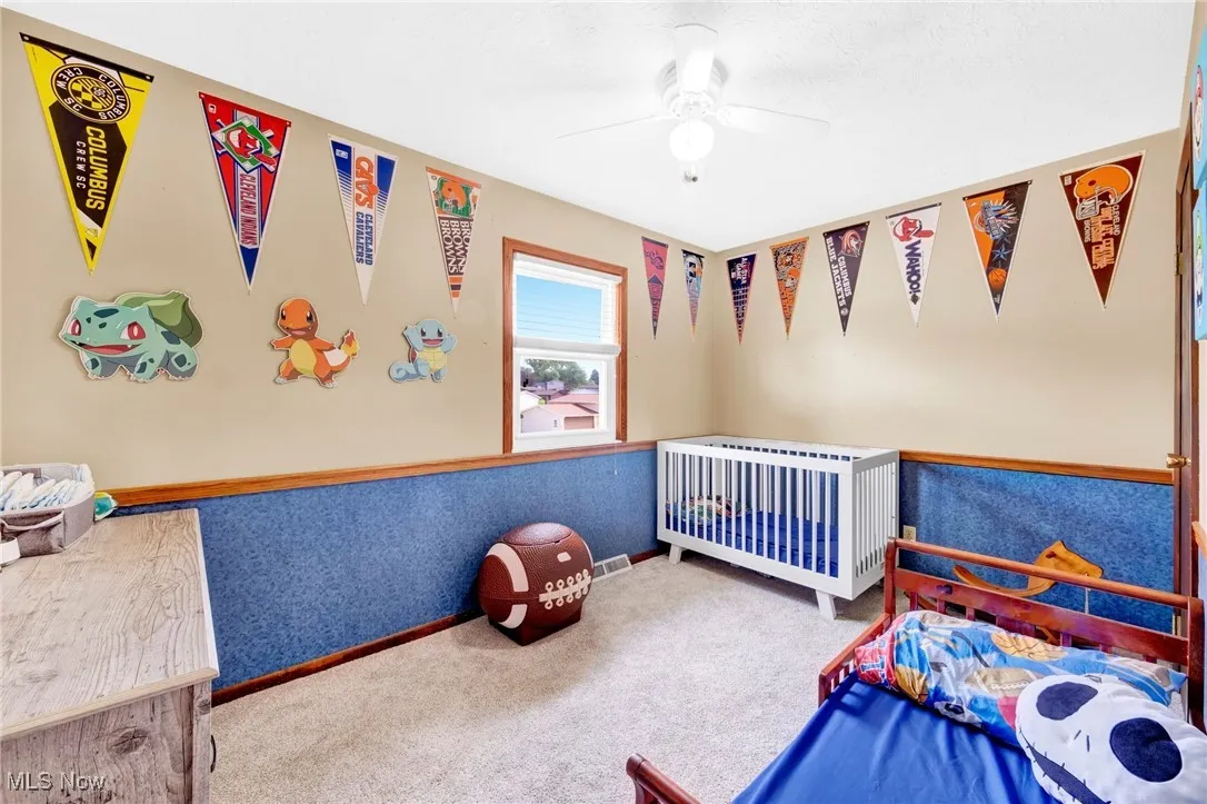 Carpeted bedroom with ceiling fan, a nursery area, and radiator