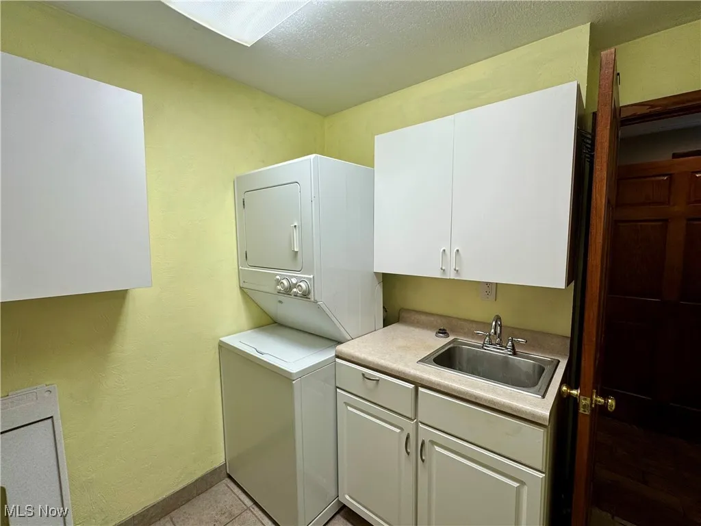 Laundry area with estacked washer and dryer, cabinet space, and light tile patterned flooring
