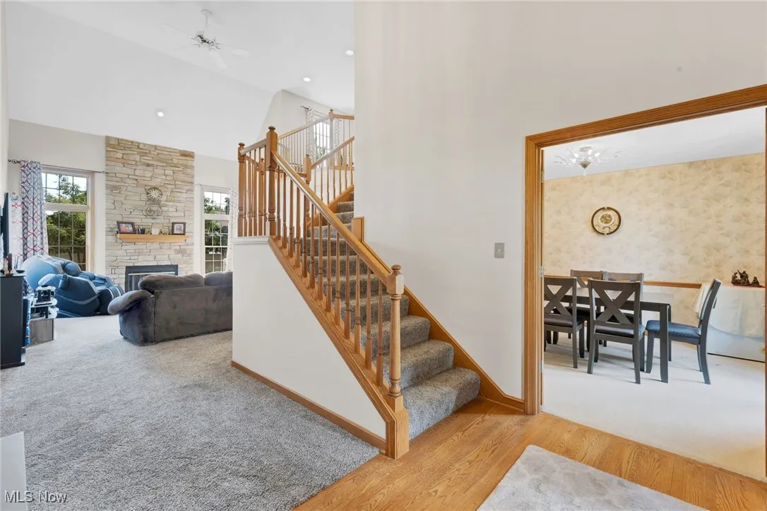 Staircase featuring wood finished floors, a fireplace, high vaulted ceiling, carpet flooring, and a ceiling fan