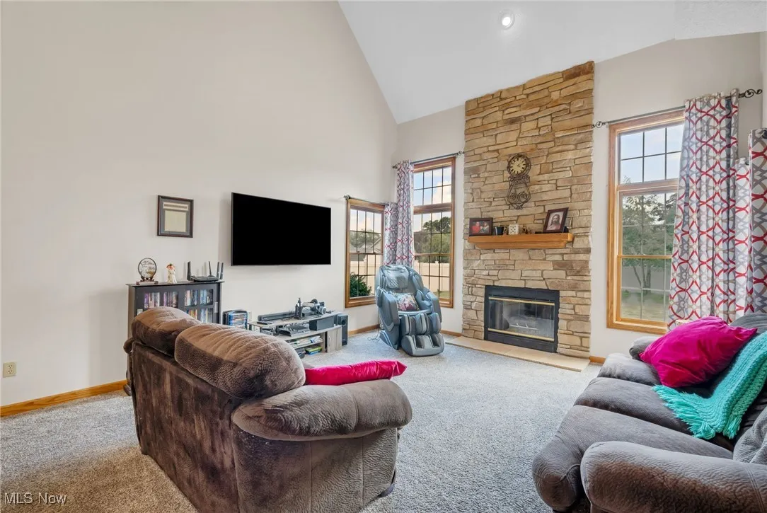 Living room featuring carpet, a stone fireplace, and high vaulted ceiling