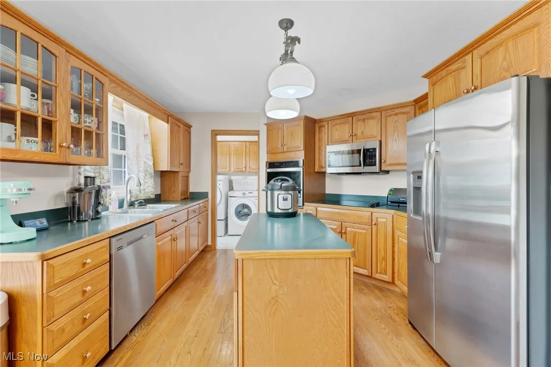 Kitchen featuring stainless steel appliances, washer and clothes dryer, a center island, light wood-style floors, and glass insert cabinets