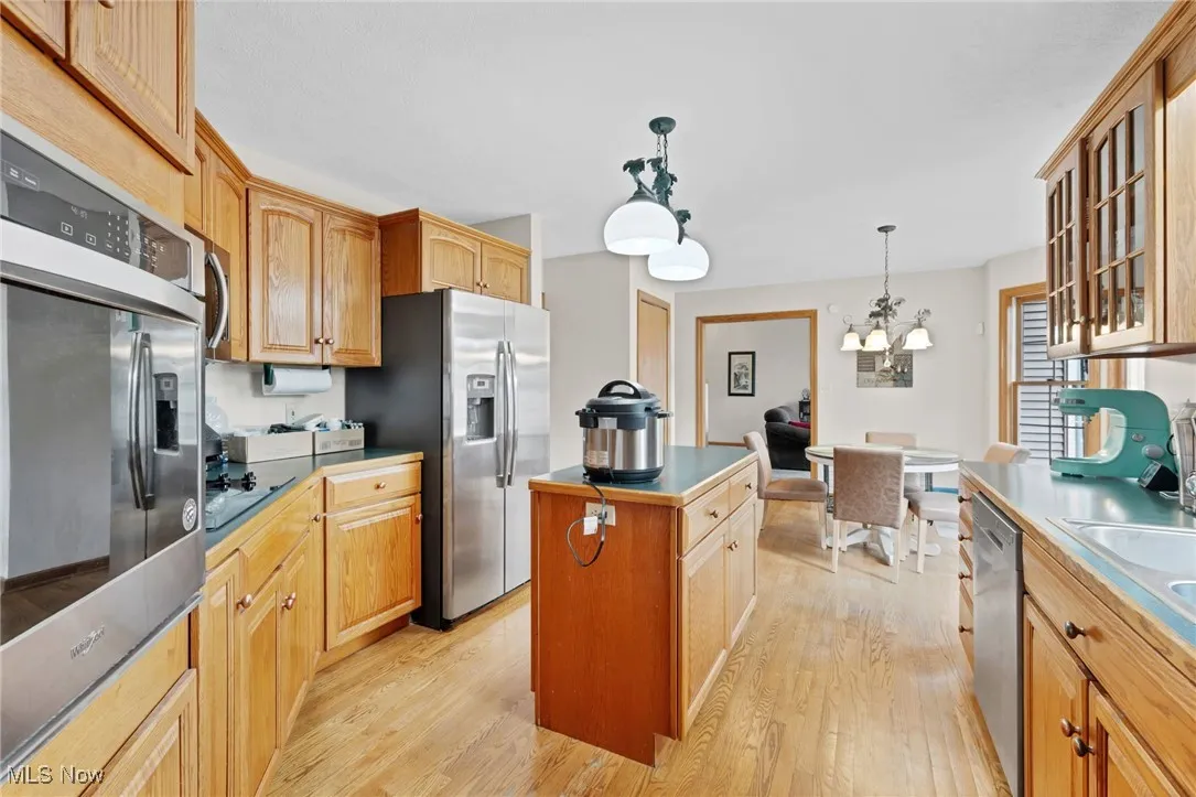 Kitchen featuring appliances with stainless steel finishes, a center island, light wood-type flooring, glass insert cabinets, and a chandelier