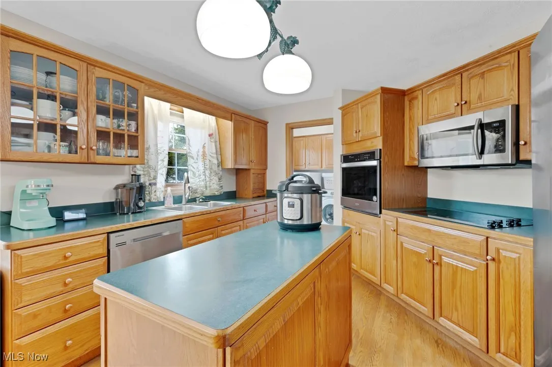 Kitchen featuring appliances with stainless steel finishes, a kitchen island, glass insert cabinets, and light wood-style floors