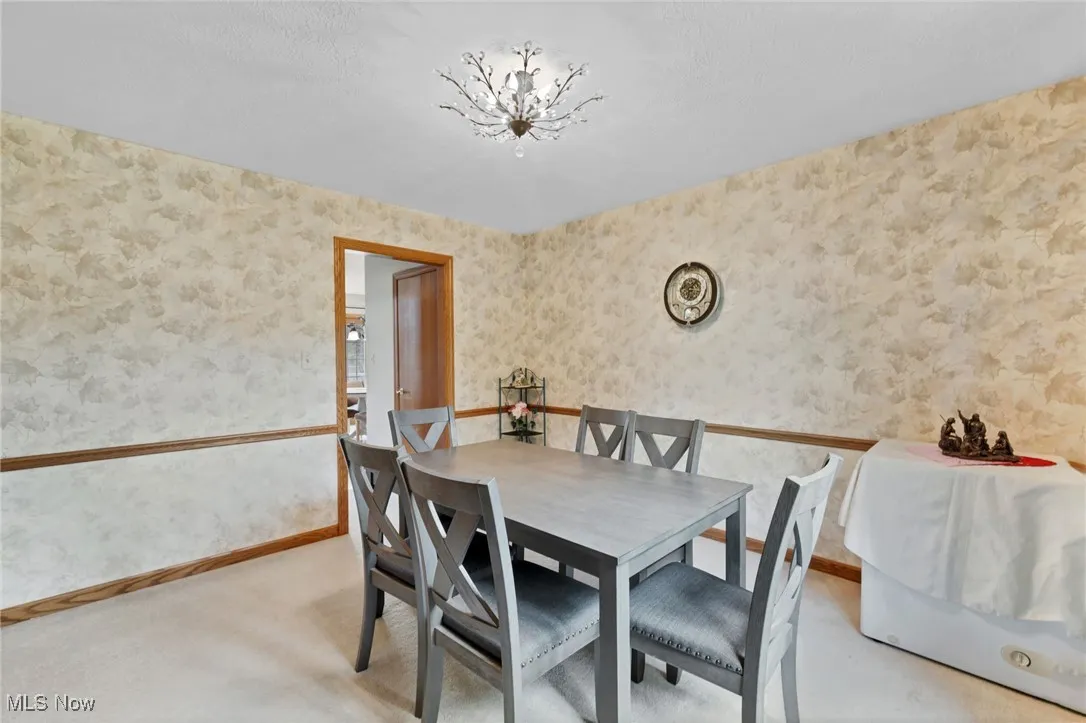 Dining area with wallpapered walls, light carpet, and a chandelier