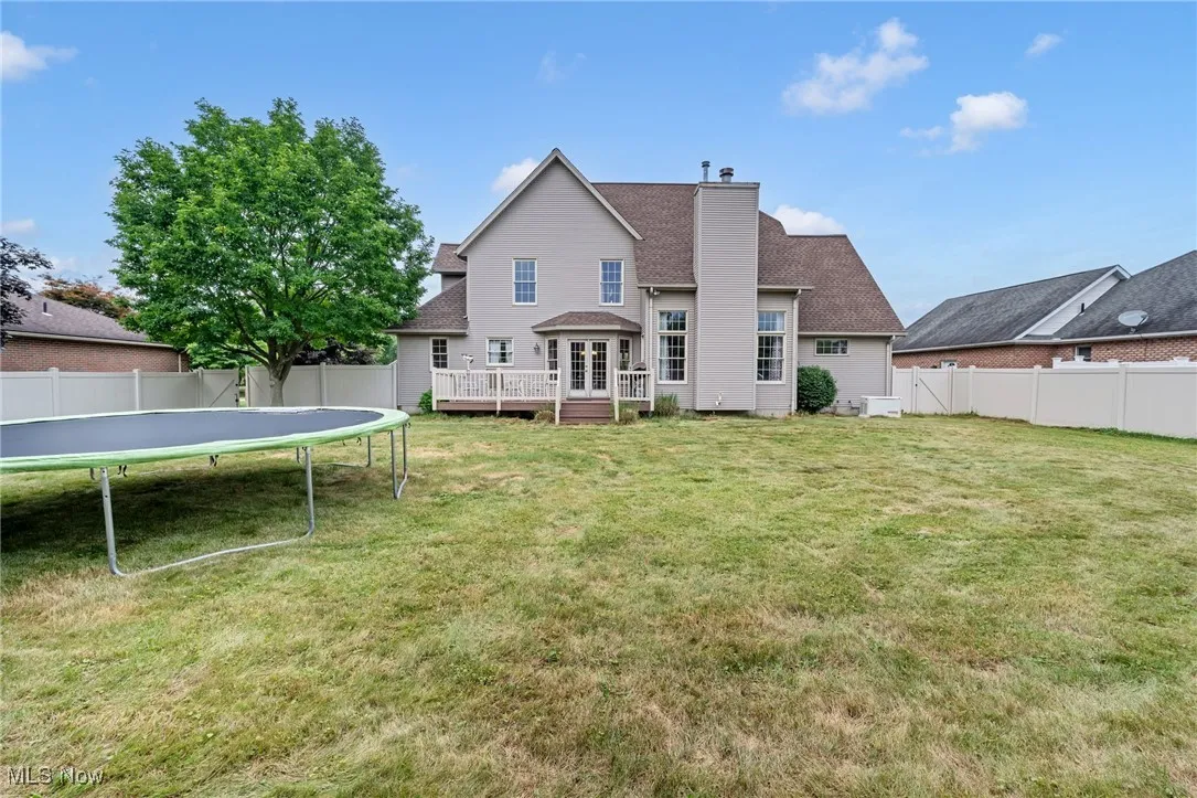 Rear view of property with a trampoline, a fenced backyard, a deck, a chimney, and a shingled roof