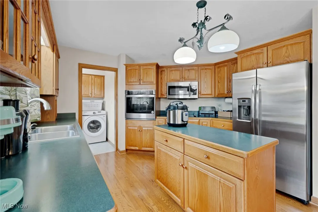 Kitchen with stainless steel appliances, washer / clothes dryer, a center island, light wood-style flooring, and hanging light fixtures