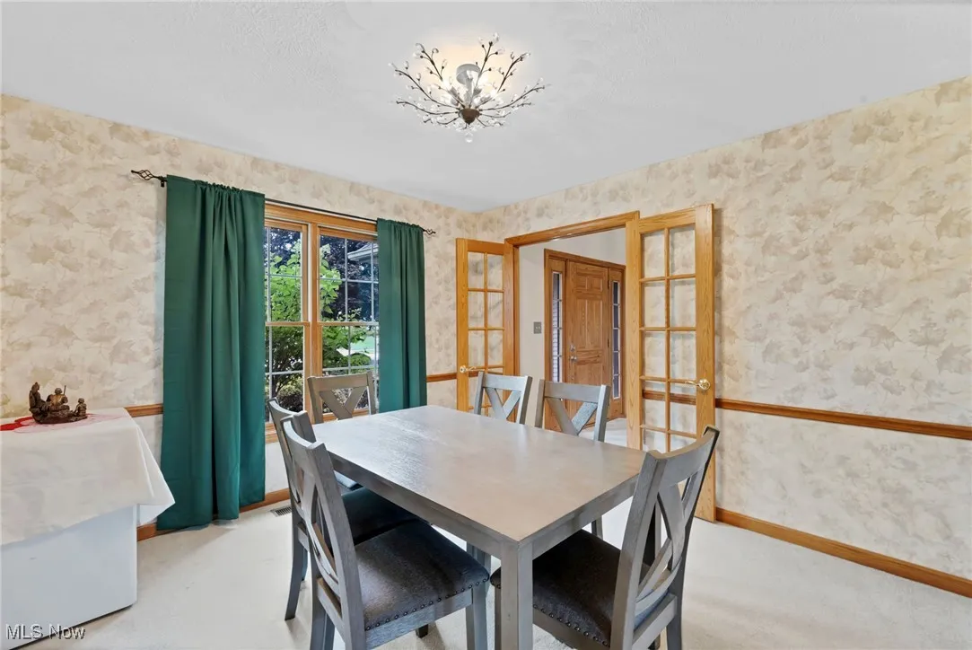 Dining room with wallpapered walls, a chandelier, and light carpet