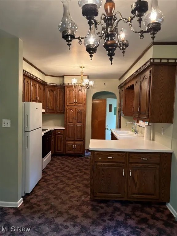 Kitchen featuring freestanding refrigerator, arched walkways, a chandelier, dark carpet, and light countertops