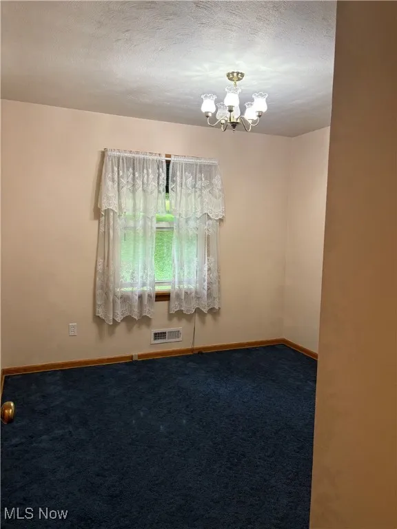 Spare room with carpet flooring, a chandelier, and a textured ceiling