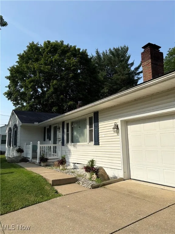 Ranch-style home with a chimney, concrete driveway, covered porch, and an attached garage