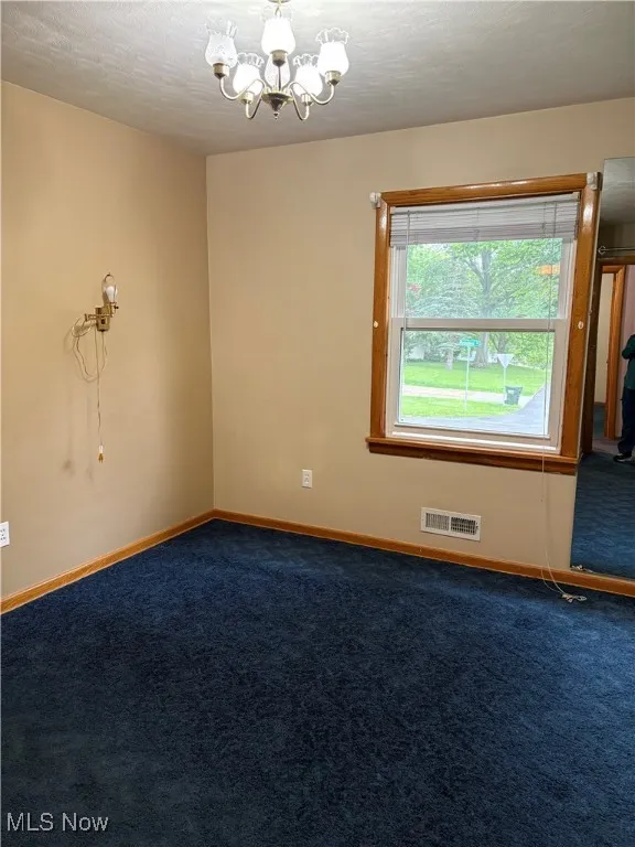 Carpeted spare room featuring a chandelier and baseboards