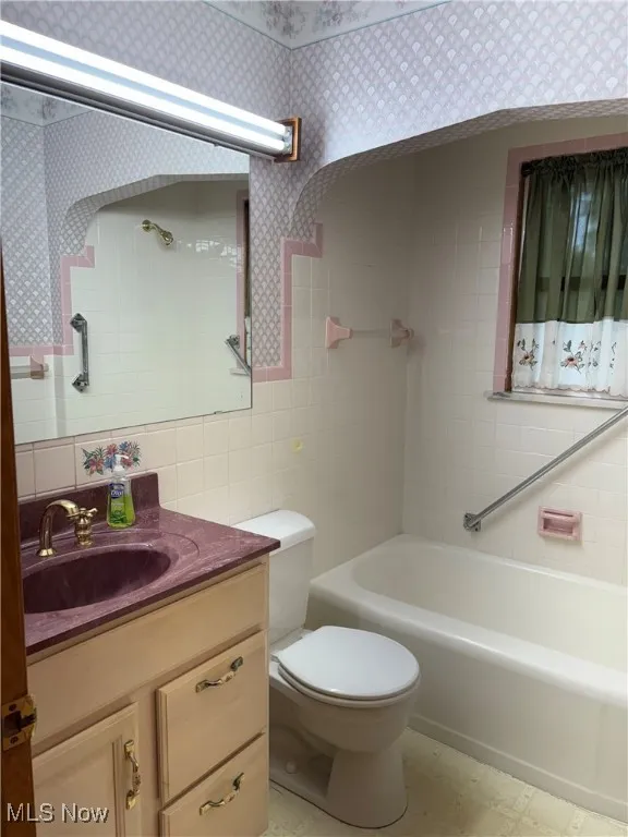 Full bath featuring tile walls, wallpapered walls, and vanity