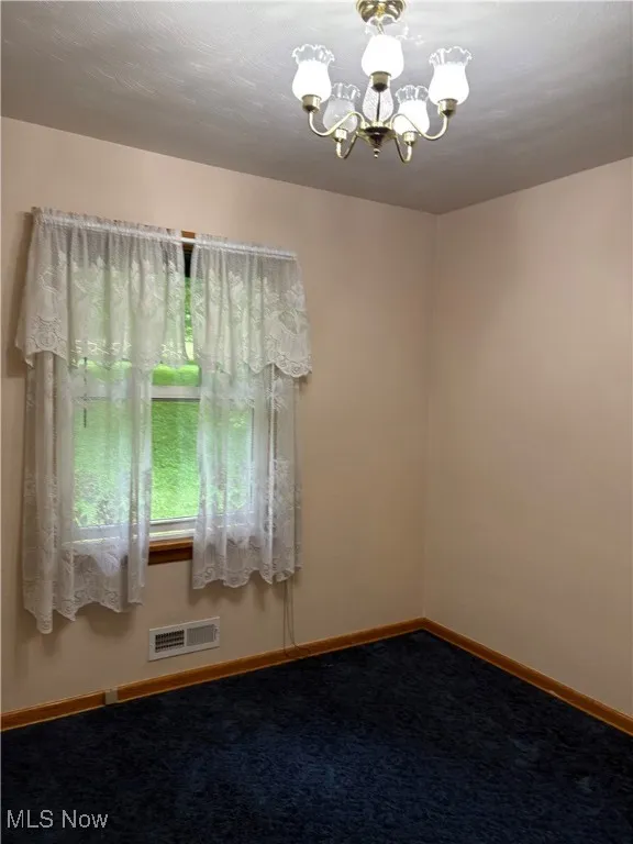 Carpeted empty room with a chandelier and baseboards