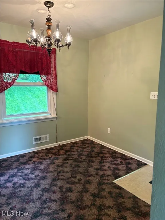 Carpeted spare room with a chandelier and baseboards