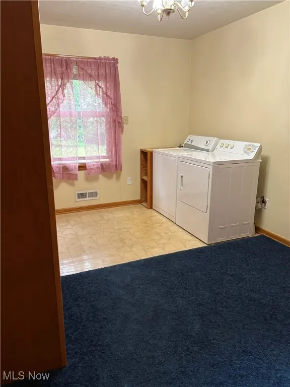 Laundry room featuring washer and dryer, a chandelier, tile patterned flooring, and carpet