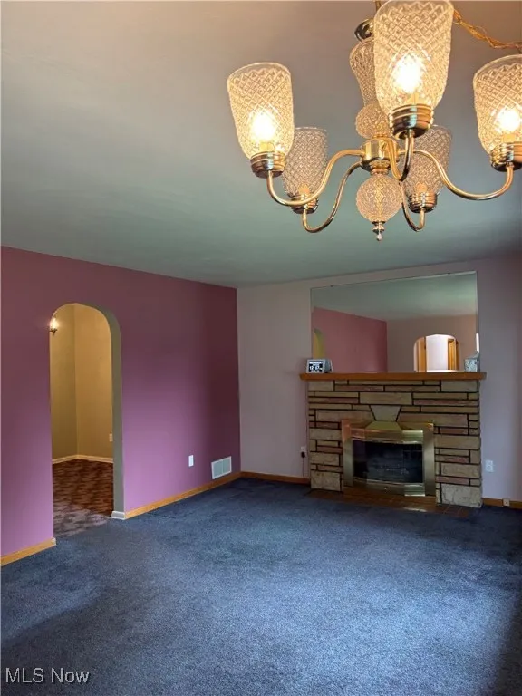 Unfurnished living room with a chandelier, carpet floors, a fireplace, and arched walkways
