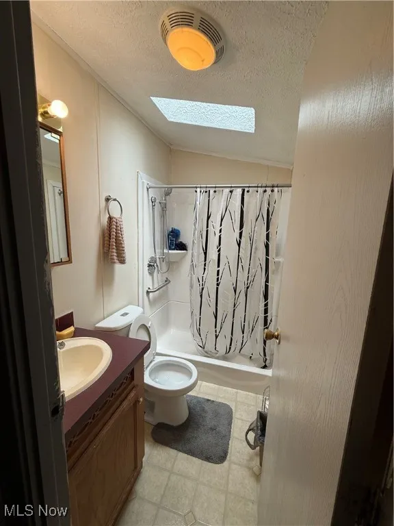 Bathroom featuring a skylight, vanity, shower / tub combo with curtain, a textured ceiling, and lofted ceiling