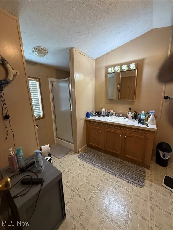 Full bathroom featuring a stall shower, vanity, a textured ceiling, and lofted ceiling
