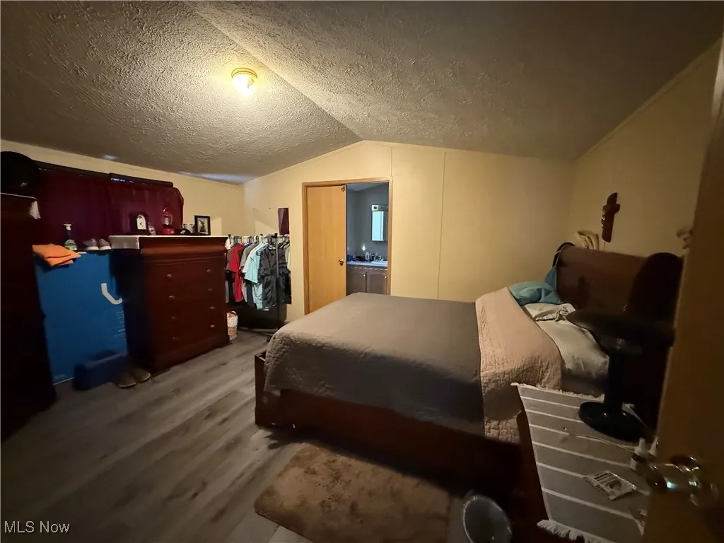 Bedroom featuring wood finished floors, a textured ceiling, and lofted ceiling