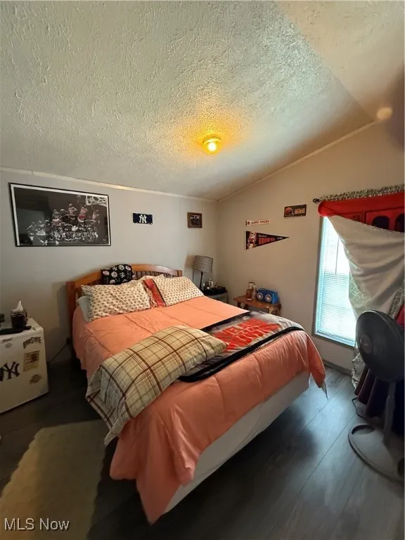Bedroom featuring lofted ceiling, a textured ceiling, and wood finished floors