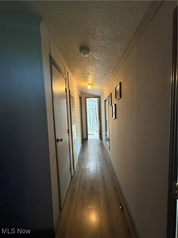 Corridor featuring a textured ceiling, ornamental molding, and light wood-type flooring