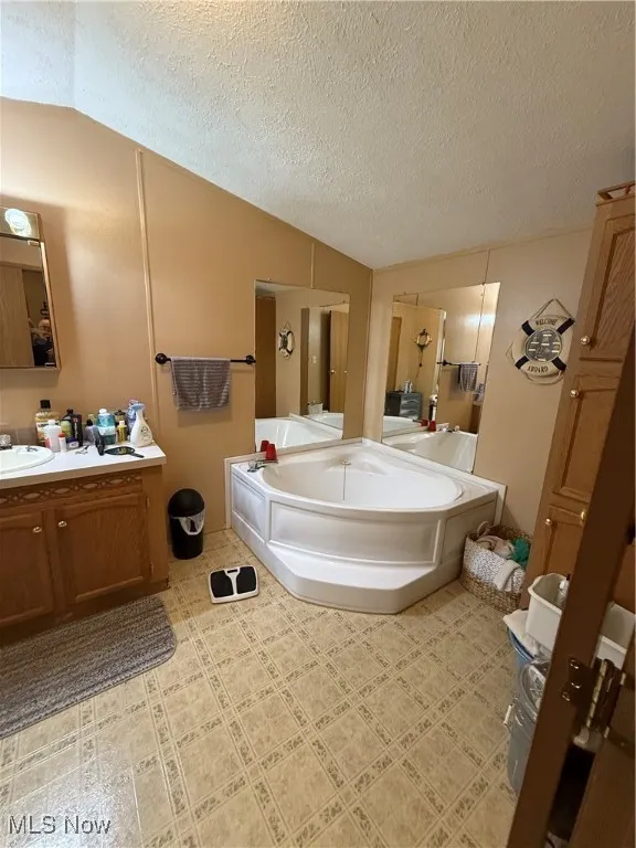 Full bathroom with lofted ceiling, a bath, vanity, and a textured ceiling