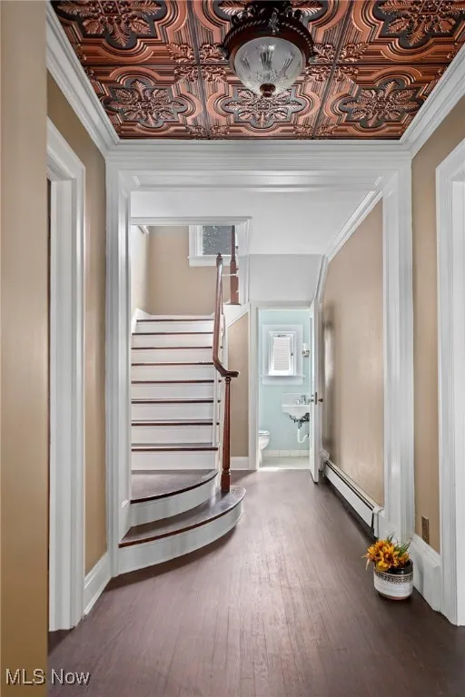 Stairway with a baseboard radiator, wood finished floors, an ornate ceiling, and ornamental molding