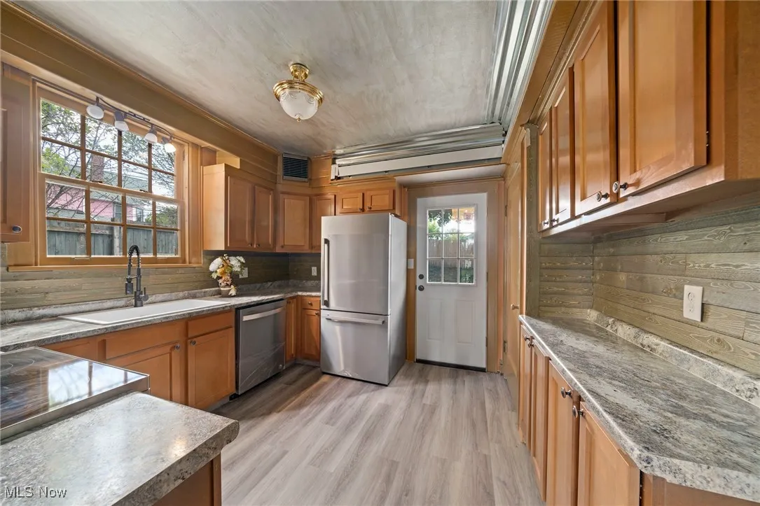 Kitchen featuring appliances with stainless steel finishes, light wood-style floors, brown cabinetry, decorative backsplash, and ornamental molding