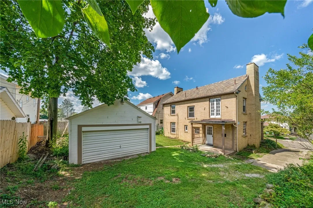 Rear view of property featuring an outdoor structure, a chimney, a detached garage, and brick siding