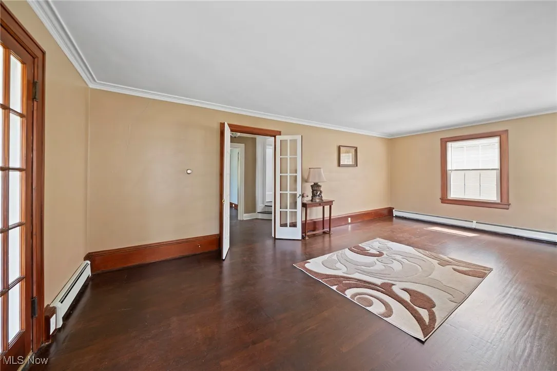 Spare room with a baseboard heating unit, wood finished floors, ornamental molding, french doors, and a baseboard radiator