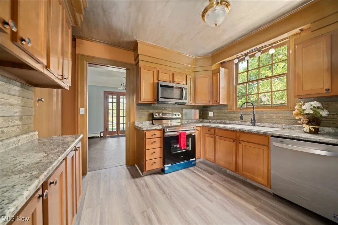 Kitchen with appliances with stainless steel finishes, light wood-style flooring, tasteful backsplash, light stone countertops, and crown molding