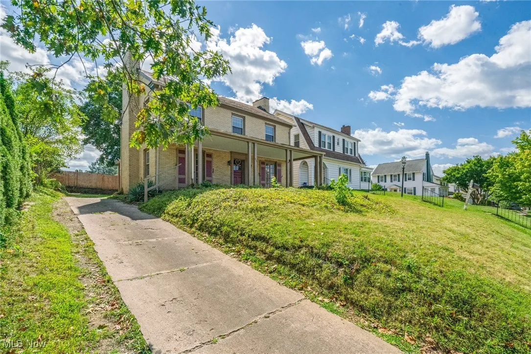 View of front of home with concrete driveway, a chimney, brick siding, and covered porch