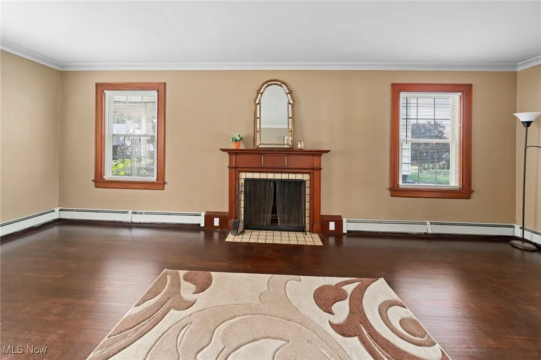Living room with wood finished floors, crown molding, a baseboard heating unit, and a tile fireplace