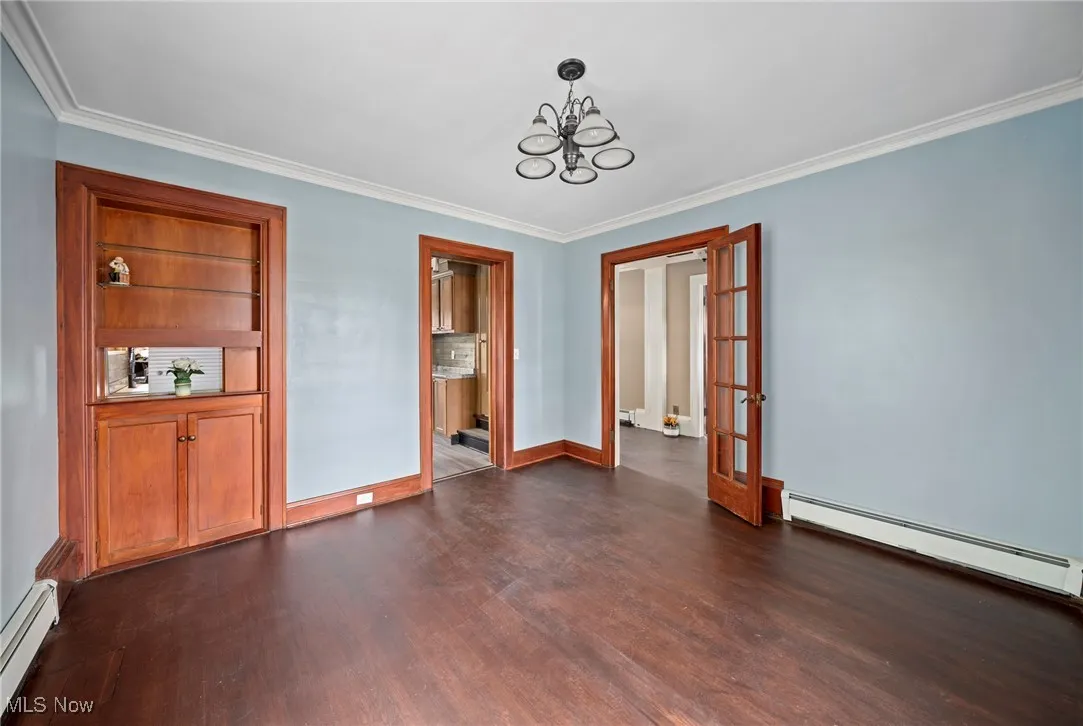 Unfurnished dining area featuring baseboard heating, french doors, ornamental molding, a chandelier, and dark wood-type flooring