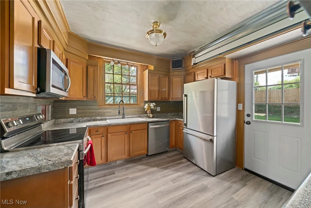 Kitchen with appliances with stainless steel finishes, brown cabinetry, tasteful backsplash, and light wood-style flooring