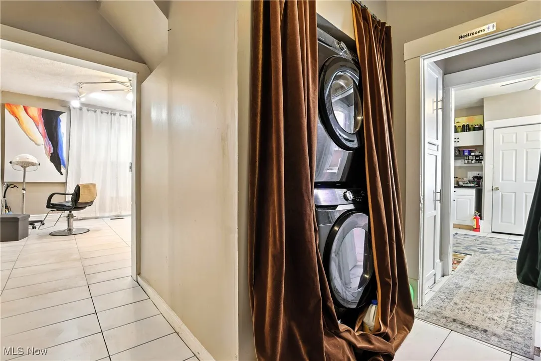 Laundry area with stacked washing machine and dryer and light tile patterned flooring