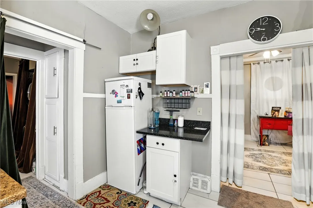 Kitchen with freestanding refrigerator, a barn door, white cabinetry, light tile patterned flooring, and dark stone countertops