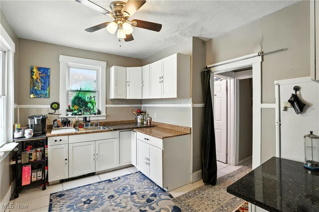 Kitchen featuring light tile patterned floors, a ceiling fan, white cabinetry, dark stone countertops, and a textured ceiling