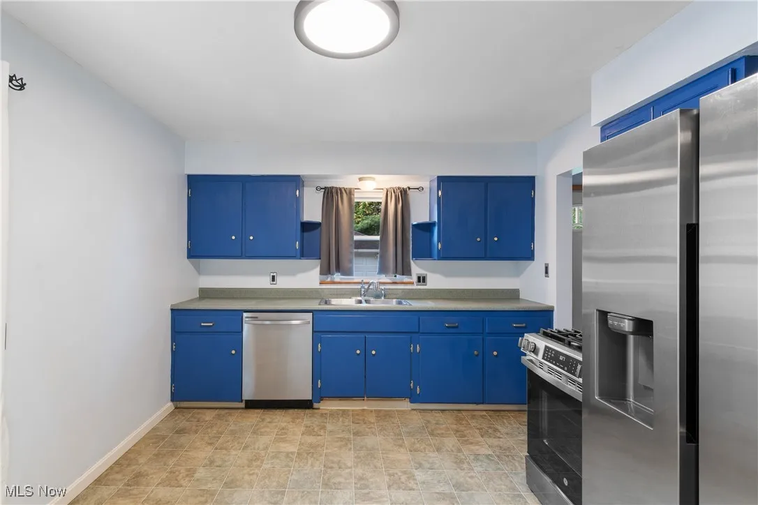 Kitchen with stainless steel appliances, blue cabinets, open shelves, light countertops, and stone finish flooring
